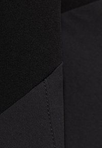 Zwarte stoffen segment met een gladde textuur, contrasterende matte en glanzende afwerkingen, en een diagonale naad met zichtbare stikdetails.