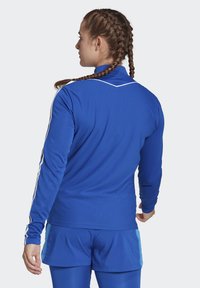 Blue athletic long-sleeve top with textured fabric, white stripe accents, and a high collar, paired with matching blue shorts.