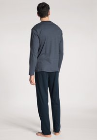 Marine gestreept langemouwen T-shirt met een ronde hals, gecombineerd met effen donkere broek, beiden in zachte stof, getoond vanuit de rug.