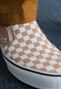 Zapatilla de lona a rayas en color arena y blanco, con suela de goma negra y un discreto detalle de logo en el lateral.