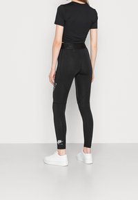 Czarne legginsy sportowe z wysokim stanem, z białym logo Nike Air na łydce i dopasowanym ściągaczem na kostkach. W połączeniu z czarną bluzką z krótkim rękawem.