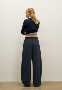 Marineblaue, weit geschnittene Hose mit elastischem Bund, kombiniert mit einem eng anliegenden Strickpullover. Glatte Textur und lockere Passform.