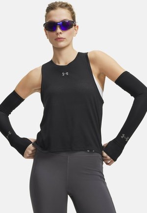 Donna con top atletico nero senza maniche, maniche nere per le braccia, leggings grigi e occhiali sportivi specchiati blu.