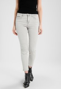 Ljust grå smala jeans med medelhög midja, slim fit och subtil slitdetalj vid knäna. Matchas med svarta ankellånga stövlar.