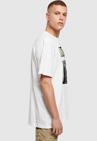 Hvid bomulds T-shirt med grafisk print, der inkluderer tekst og billede. Korte ærmer, afslappet pasform, rund halsudskæring, glat tekstur.
