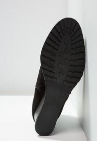 Botte en daim noir avec une semelle texturée, présentant un motif de bande de roulement prononcé et une fermeture éclair latérale. Le talon est bas et arrondi.