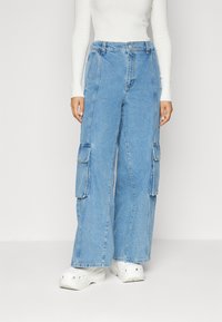 Lysblå denim cargo bukser med brede ben, der har store sidelommer og en afslappet pasform. Bæres med hvide fodtøj.