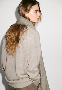 Jasnobrązowy, oversize sweter o miękkiej fakturze, z okrągłym dekoltem i opuszczonymi ramionami, w komplecie z dopasowanym szalikiem.