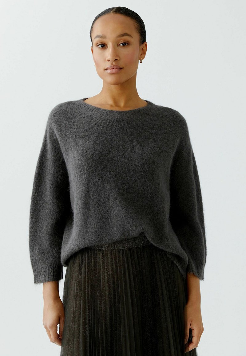Gray, oversized sweater made from soft, fuzzy material with a round neckline and loose sleeves, paired with a pleated black skirt.