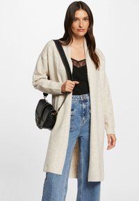 Krämfärgad stickad cardigan med öppen front, texturerad tyg, långa ärmar och sidofickor, ihop med en svart top och högmidjade jeans.