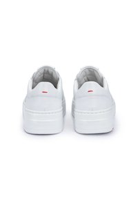 White leather sneakers with a smooth texture, featuring a chunky sole and subtle red stitching accents on the heel.