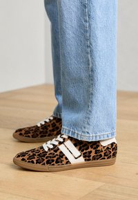 Tenisky s leopardím vzorem, hnědým a černým semišem, bílými tkaničkami a béžovou gumovou podrážkou. Nosené s světle modrými jeansy s ohrnutými nohavicemi.