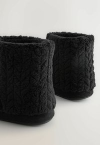 Mustad musta fliisi põlvevahed, millel on tekstureeritud nöörmustri muster, pehme sisetald ja lame must välistald. Lihtne, ümmargune kuju ilma kaunistusteta.