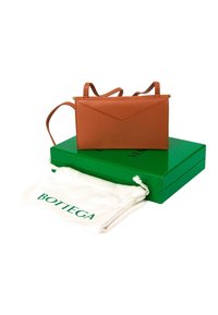 Sac à main en cuir marron avec double bandoulière sur une boîte verte à côté d'un sac à poussière blanc à cordon avec le logo Bottega en lettres vertes.