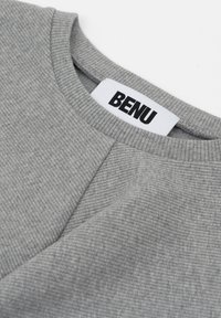 Szary, prążkowany materiał swetra z okrągłym dekoltem oraz etykietą "BENU" widoczną w czerni na białym tle.