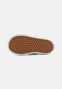 Suela de zapato de goma con textura de panal, que presenta un patrón de rodadura marrón, borde blanco y pequeños acentos verdes y rojos.
