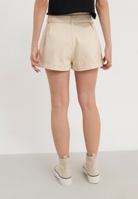 Beige pielēti šorti ar apgrieztu apakšmalu un priekšējo krokām. Valkāti ar gaiši beigu potīšu zābakiem ar baltu zoli.