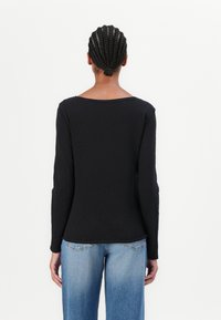 Black long-sleeve top with a wide neckline and textured fabric, paired with light blue jeans, viewed from the back.