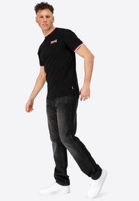 Must värviline lühikeste varrukatega t-särk punase ja valge triibulise krae ning rinnal logo. Tumedad teksad ja valged spordikingad.