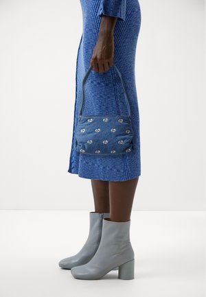 Blå mönstrad handväska i texturerat tyg med silverdetaljer med logotyp, matchad med ljusgrå ankelboots och en ribbad blå klänning.