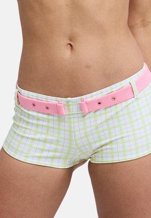 Zbliżenie na środkową część ciała osoby noszącej jasnożółte i różowe szorty w kratę z różowym paskiem i odsłoniętym brzuchem.