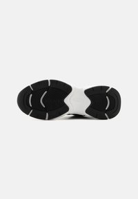 Semelle de sneaker noir et blanc en matériau en caoutchouc, avec un design de bande de roulement texturé et un motif distinct avec la marque "KARL" embossée.