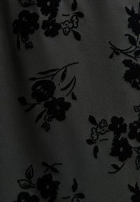 Czarna koronkowa aplikacja z florystycznym wzorem na przejrzystym czarnym materiale, z misternie wyhaftowanymi kwiatami i liśćmi, tworząc teksturowany i wielowarstwowy efekt.