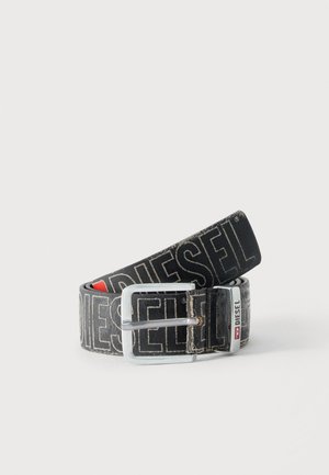 Cinturón negro Diesel con gran texto de logo en blanco, hebilla rectangular plateada y detalle de la anilla metálica con marca, enrollado sobre un fondo claro.