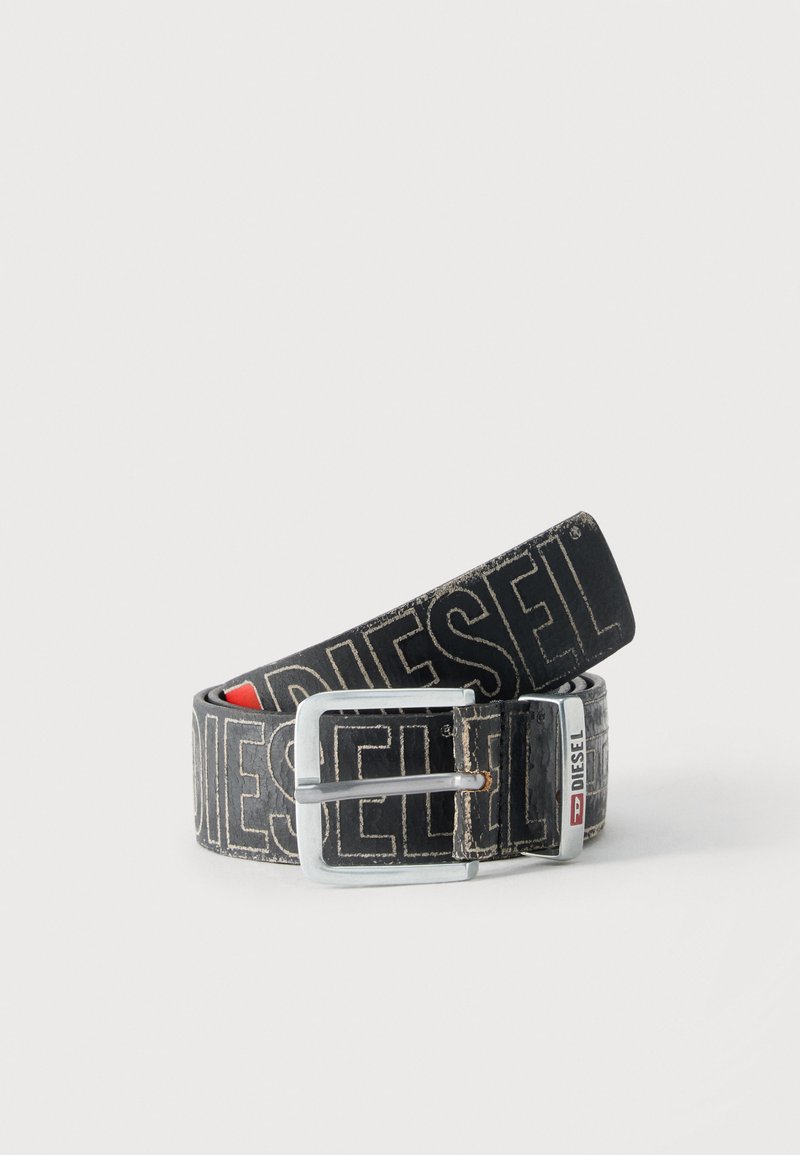 Μαύρη ζώνη Diesel με μεγάλο λευκό λογότυπο, ορθογώνια ασημένια αγκράφα και μεταλλική λεπτομέρεια με χαρακτηριστικό σήμα, τυλιγμένη σε ανοιχτό φόντο.