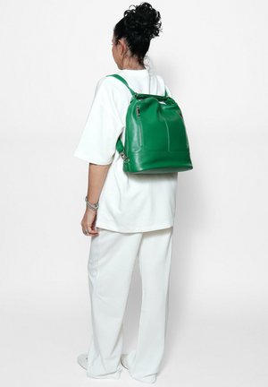 Sac à dos en cuir vert avec des bretelles ajustables, texture lisse, poches frontales et un sommet arrondi orné d'un accent métallique.