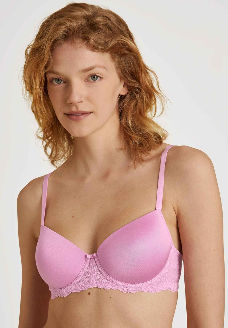 Lichtroze gewatteerde beha met kantaccenten, voorzien van verstelbare bandjes en een gladde bovenkant. Het kant voegt een gestructureerde detail toe onder de cups.