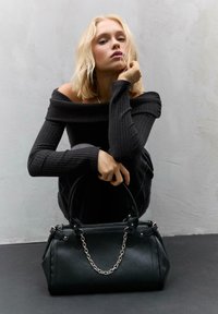 Sac à main en cuir noir avec une forme structurée, accent en chaîne argentée et doubles poignées. La texture de surface semble lisse avec des détails de couture.
