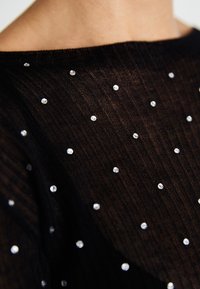 Schwarzes, geripptes Strickoberteil mit verstreuten klaren Edelsteinen als Verzierung. Texturiertes Material mit weitem Ausschnitt und kurzen Ärmeln.