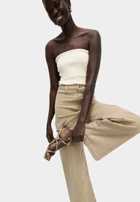 Beige široké kalhoty, bílé žebrované bezramínkové tričko a sandály na podpatku se vzorem hada, zdůrazňující materiály a vzory.