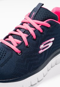 Jūras spēku tīkla sporta apavi ar rozā šņorēm un baltu gumijas zoli. Ir logo detaļa malā un teksturēts augšdaļa, lai nodrošinātu gaisa caurlaidību.