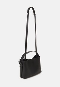 Czarna skórzana torba na ramię o minimalistycznym designie, z długim paskiem i otwartą górą. Gładka tekstura bez widocznych elementów metalowych.