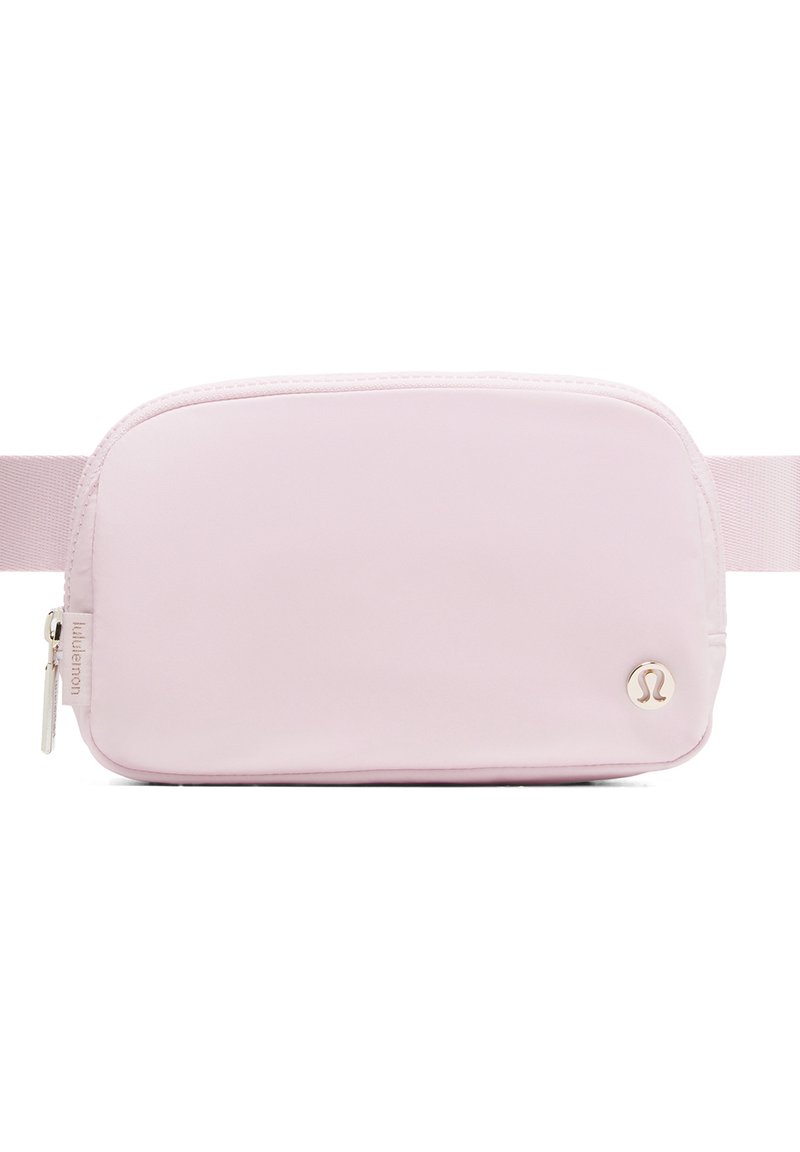 Roza tkaninska pasna torba z gladko teksturo, pravokotne oblike, z zadrgo in majhnim kovinskim logotipom spredaj. Vključeni so tudi nastavljiv trak.