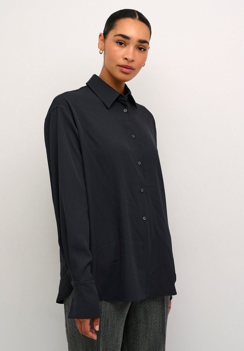Zwarte lange mouwen blouse met kraag, gladde textuur en een comfortabele pasvorm. Voorzien van zwarte knopen en opgerolde mouwen.