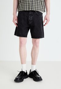 Sorte denim shorts med en afslappet pasform, syet kant og sidelommer. Parret med sorte polerede sko og hvide ankelstrømper.