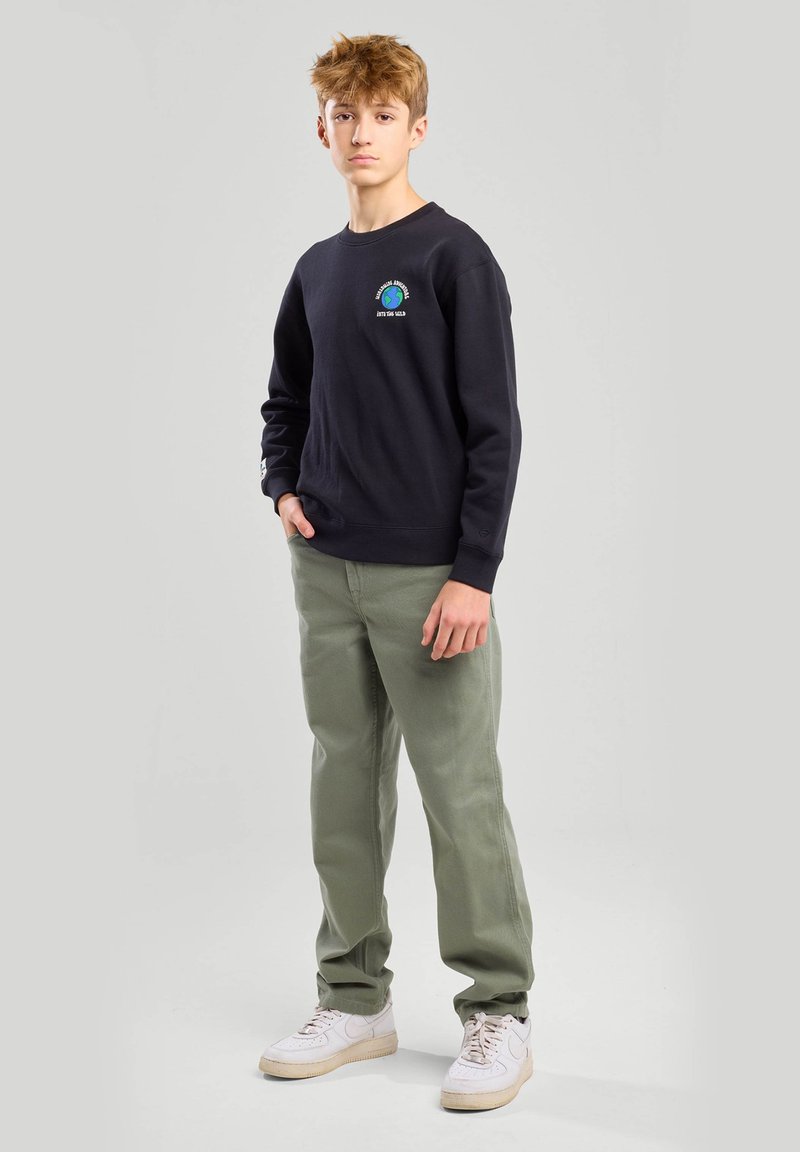 Mustapaitainen huppari, jossa on pieni logo rinnassa, yhdistettynä vihreisiin housuihin ja valkoisiin lenkkikenkiin. Kangas näyttää pehmeältä ja rentolta.