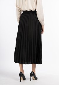 Schwarzer, plissierter Rock mit elastischem Bund, kombiniert mit schwarzen High Heels. Glattes Material mit vertikaler Textur und fließendem Design.