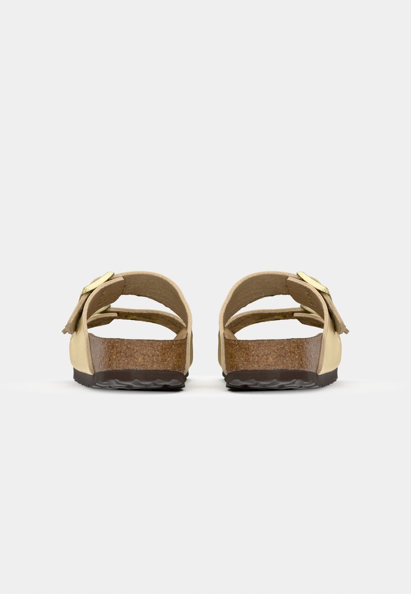 Gelbe Sandalen mit einem Korkfußbett, verstellbaren Riemen und einer schwarzen Gummisohle. Auffälliger Schnallenakzent an der Seite. Rückansicht dargestellt.