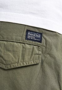 Shorts cargo vert olive avec une poche arrière portant une étiquette bleue qui indique "Petrol Ind DENIM DRIVEN SINCE '89 FLORIDA U.S.A."