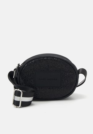 Sac à bandoulière noir en forme d'ovale avec une surface texturée, présentant un patch logo mat et une bandoulière réglable rayée. Accents en satin et en cuir.