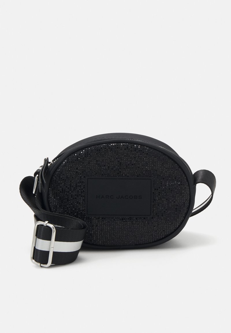 Sac à bandoulière noir en forme d'ovale avec une surface texturée, présentant un patch logo mat et une bandoulière réglable rayée. Accents en satin et en cuir.