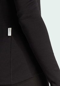Maglietta nera a maniche lunghe con un design aderente. Presenta un piccolo etichetta Terrex visibile sulla cucitura laterale e un tessuto morbido e texturizzato.