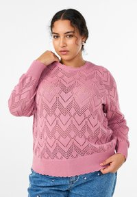 Rozā adīts džemperis ar zīda rakstu, apaļu kakla izgriezumu un ribām ap pogu galiem. Brīvs piegriezums un teksturēts, izgatavots no viegla materiāla.