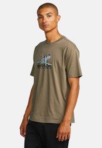 Olive green cotton t-shirt with a crew neck, short sleeves, and a butterfly graphic print on the front, paired with black pants.