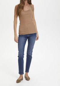 Brun ribbad linne med rundad halsringning, tillsammans med mörkblå slim-fit jeans och ljusbruna ballerinas. Mjuk textur och lätt volangnärm.