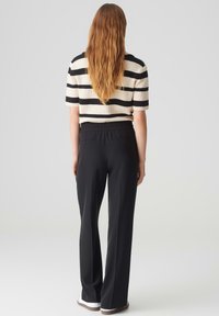 Gestreiftes Strickoberteil in Creme und Schwarz, kombiniert mit hochgeschnittenen schwarzen Hosen, die einen elastischen Bund und Seitentaschen haben.